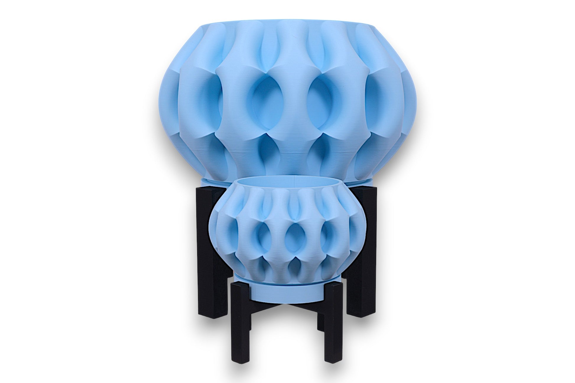 Two light blue PLA planters – 3D printed with oval dimple textures and rounded forms, displayed on black four-legged stands
