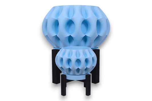 Two light blue PLA planters – 3D printed with oval dimple textures and rounded forms, displayed on black four-legged stands
