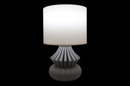 Table lamp with a white shade and decorative base on a black background
