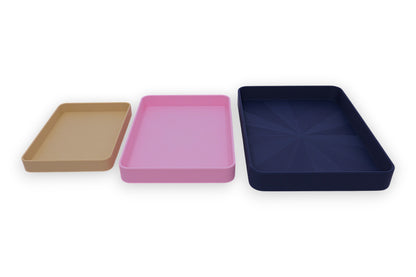 Three rectangular trays in brown, pink, and navy on a white background