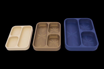Three compartmentalized trays in beige, brown, and blue on a black background