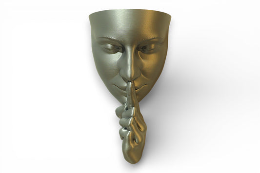 Metallic 3D‑printed wall sculpture of a stylized face with raised finger in a shushing gesture