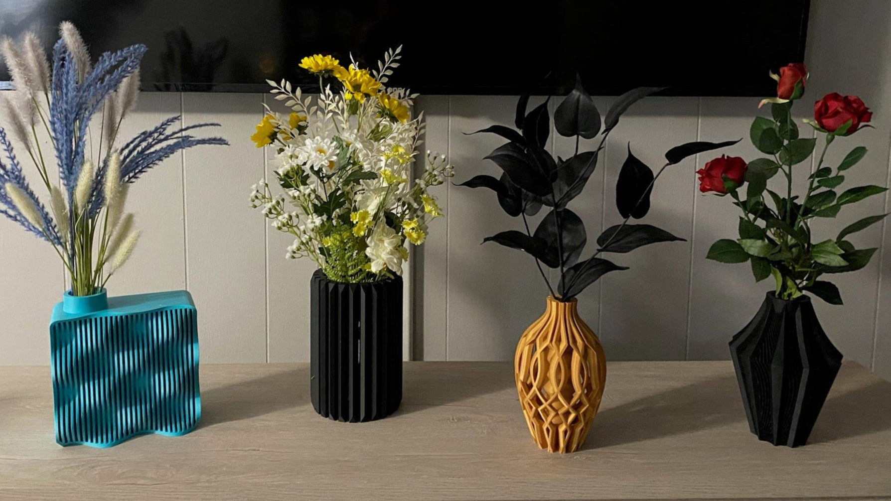 Four vases with artificial plants on a table in front of a television.