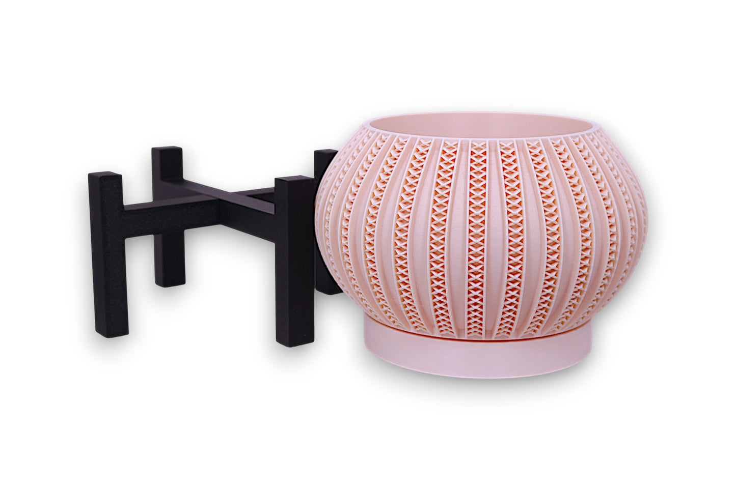 Blush pink planter with repeating X-shaped cutouts on black four-legged stand