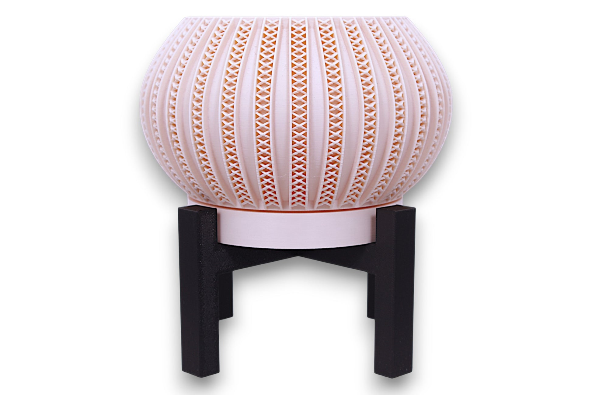 Blush pink planter with repeating X-shaped cutouts on black four-legged stand