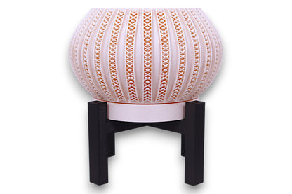 Blush pink planter with repeating X-shaped cutouts on black four-legged stand